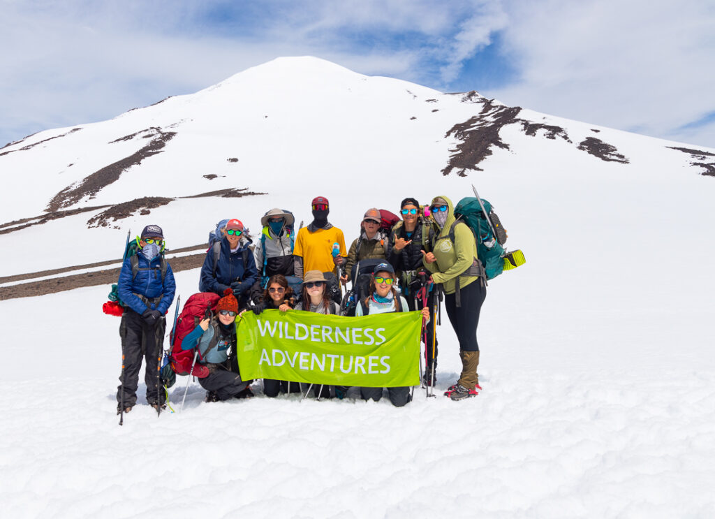 Group of students mountaineering holding a green flag that says Wilderness Adventures.