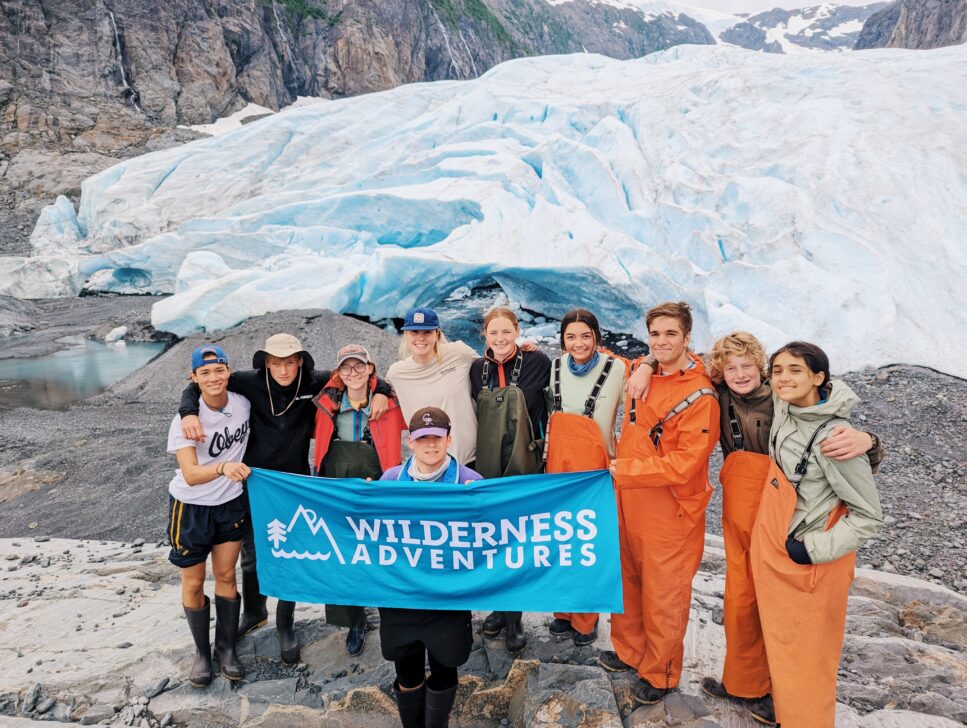 Group of students holding up a Wilderness Adventures banner in front of glacial ice