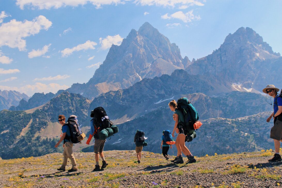 Group of students backpacking in front of large jagged mountains.
