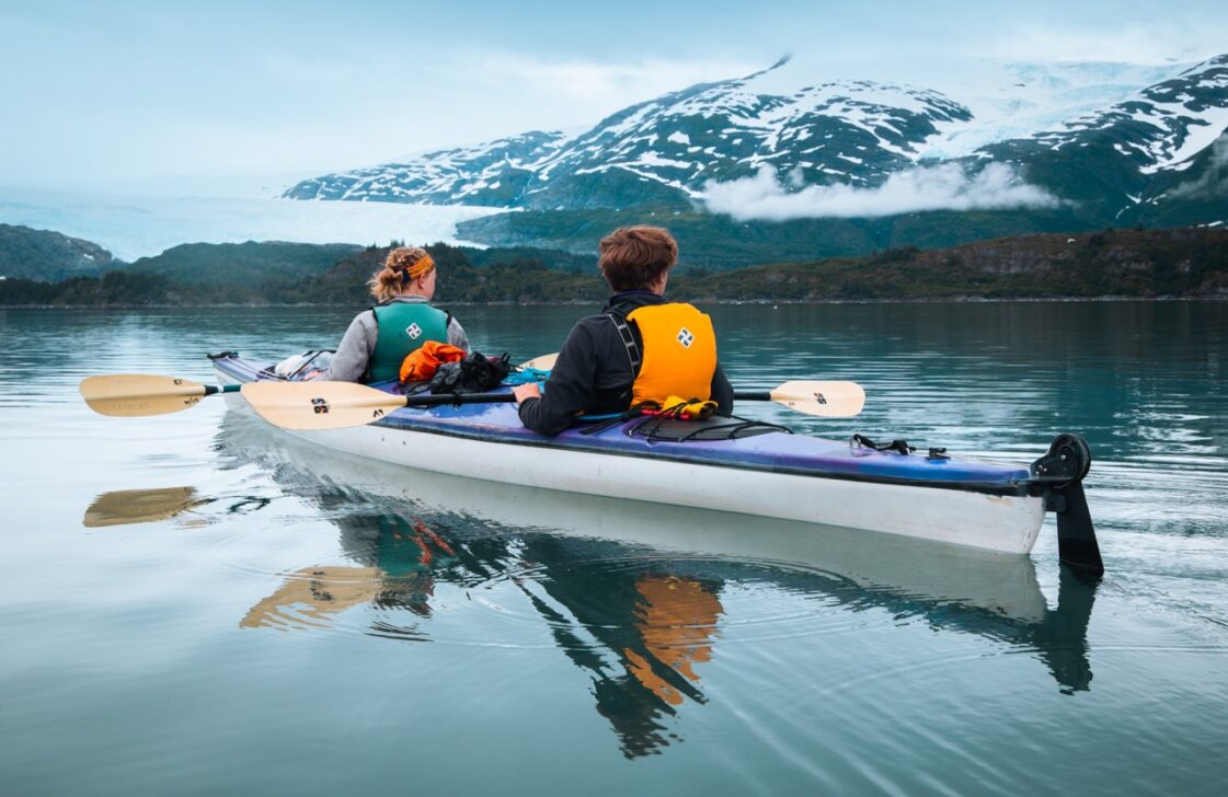 Two people looking to the horizon of mountains while kayaking on smooth water.
