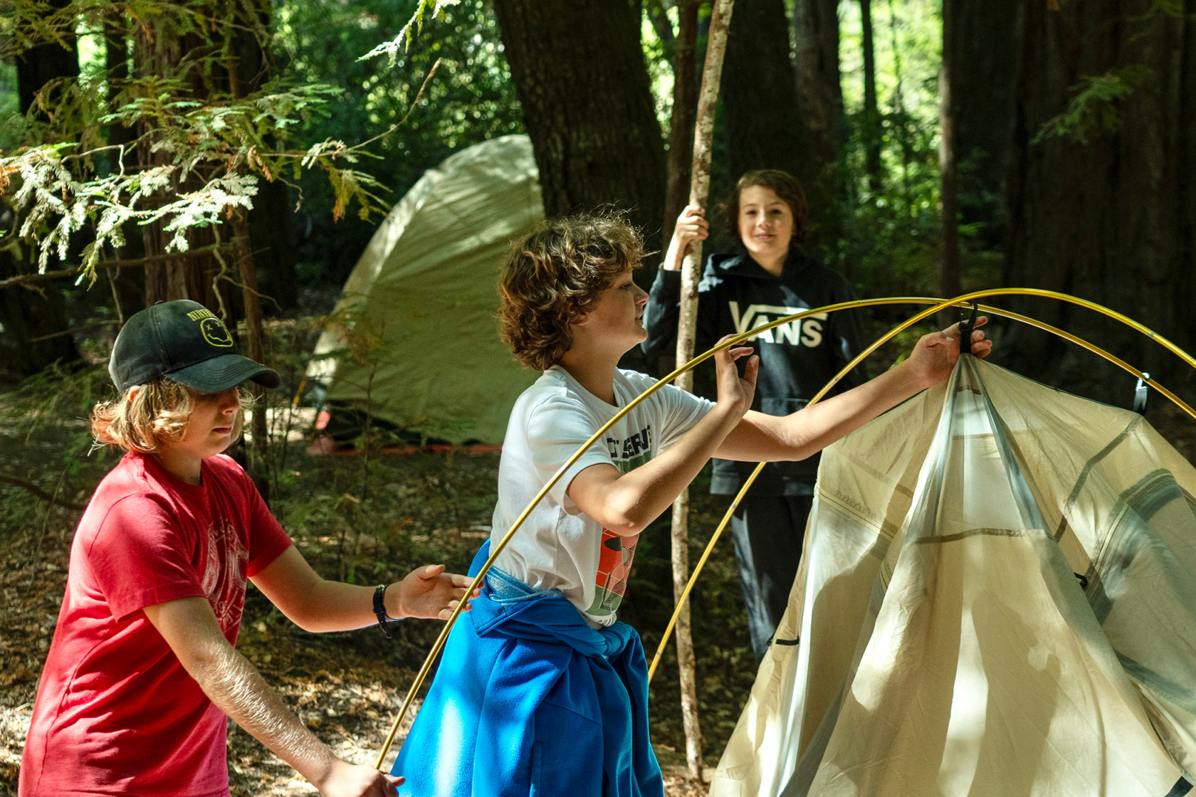 Three campers working together to set up a tent in the woods.