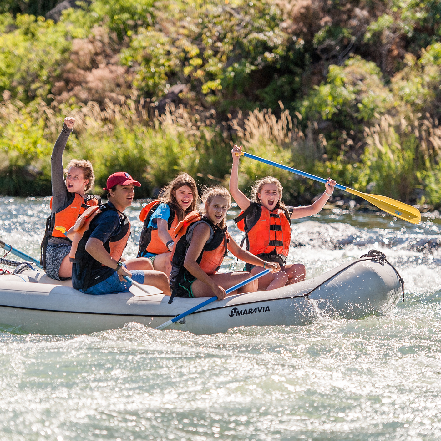 Group of campers on an inflatable raft floating down the river with excited looks on their faces.