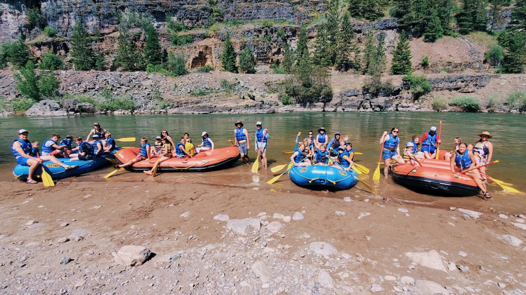 four rafts full of campers on the shore of the river looking excited.