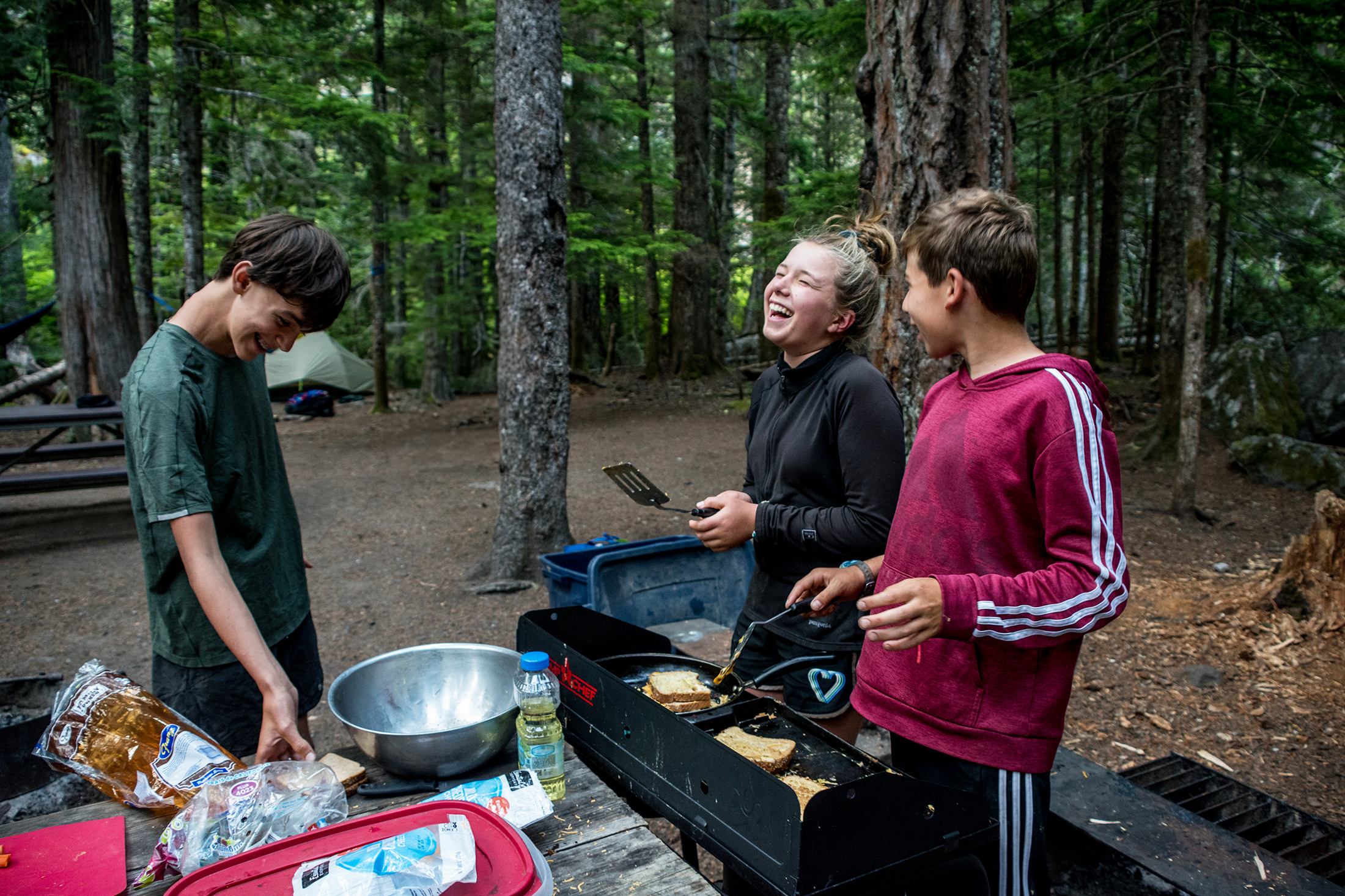 Thee people cooking french toast at a camp stove and laughing.