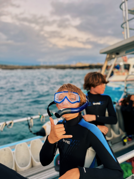 Young boy with a snorkeling mask on standing on a boat in Hawaii.
