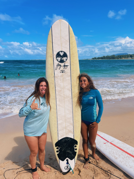 Two girls next to a surfboard on a beach in Hawaii.