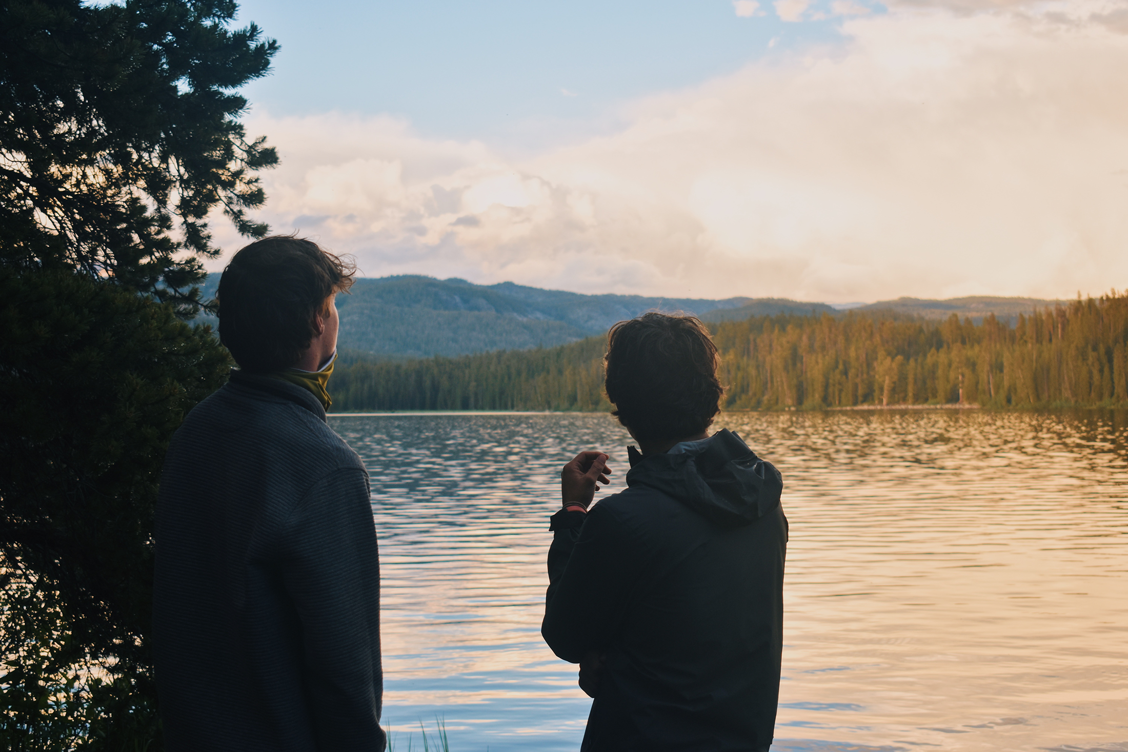 Two people looking out at a lake at sunset. 