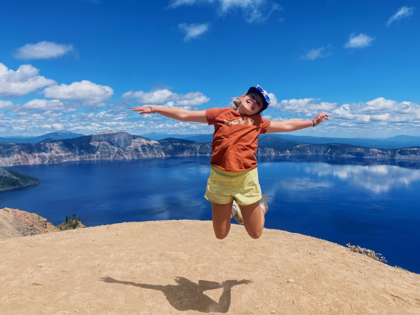 Girl jumping in the air in front of a big blue lake.
