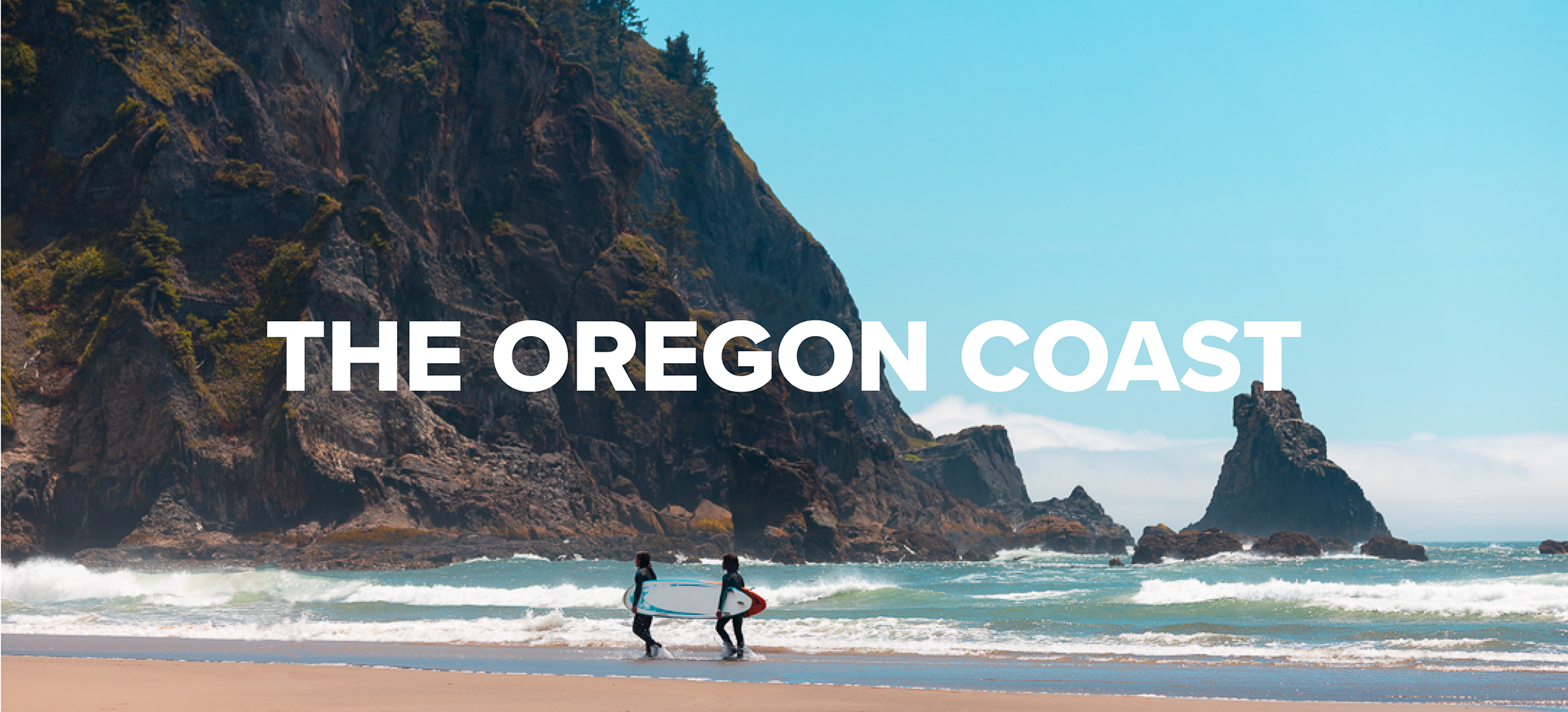 The Oregon Coast with two surfers carrying surfboards together. 